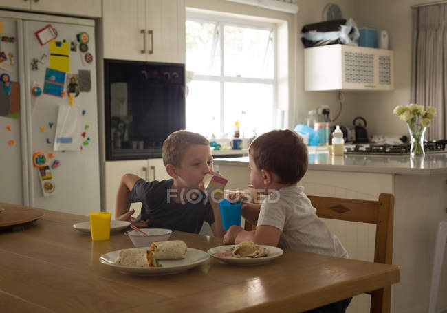 Frères et sœurs qui prennent le petit déjeuner sur une table à manger à la maison — Photo de stock
