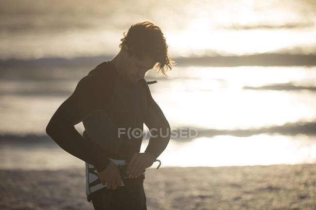 Surfista masculino vestindo cinto na praia ao entardecer — Fotografia de Stock