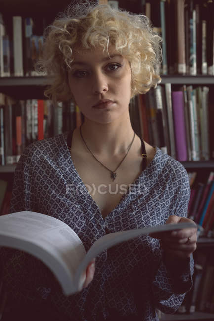 Portrait of young woman holding a book in library — Stock Photo