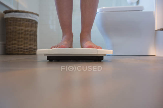 Низкая часть женщины проверяет свой вес на весах дома — стоковое фото