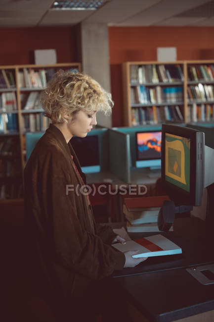 Giovane donna che tiene un libro in biblioteca — Foto stock