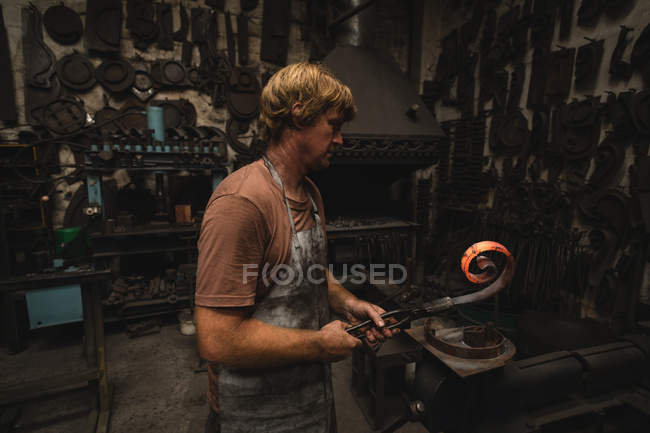Forgeron façonnant une tige de métal en atelier — Photo de stock