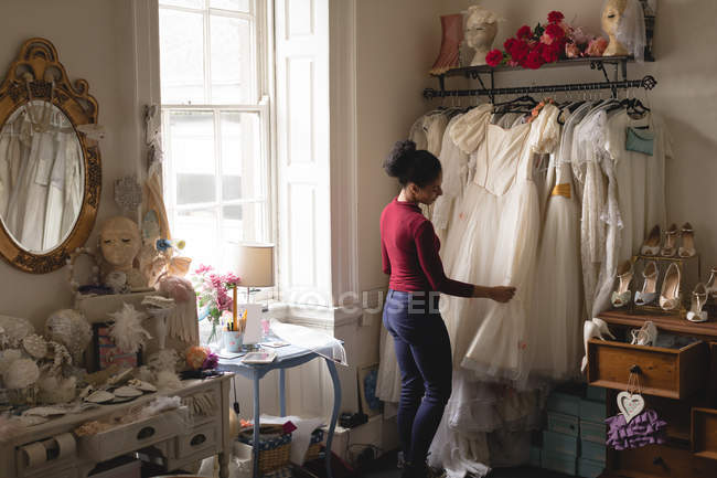 Woman selecting wedding dress from clothes hangers at boutique — Stock Photo