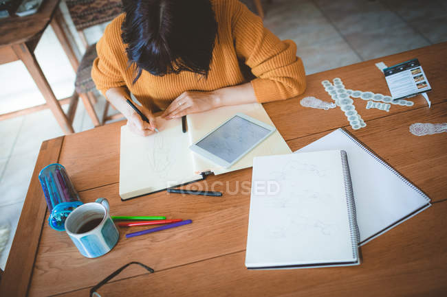 Femme dessinant un croquis dans un livre à la maison — Photo de stock