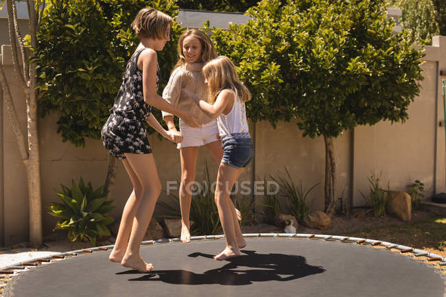 Frères et sœurs sautant sur le trampoline dans le jardin par une journée ensoleillée — Photo de stock