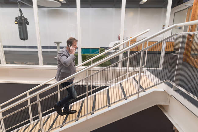 Бізнес-леді розмовляє по мобільному телефону під час прогулянки нагору в офісі — стокове фото