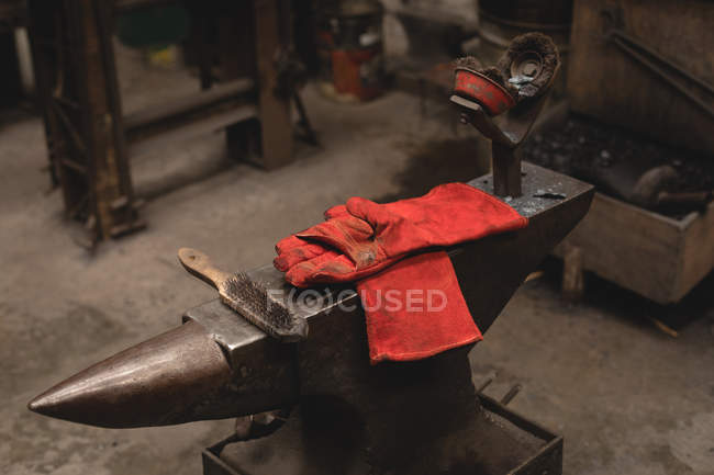 Spazzola metallica a mano e guanti su incudine in officina — Foto stock