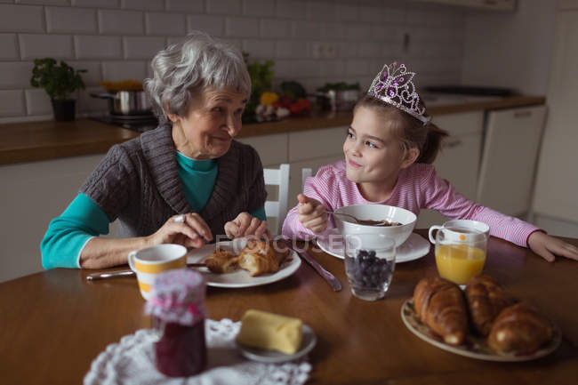 Grandmother and granddaughter having breakfast in kitchen at home — Stock Photo