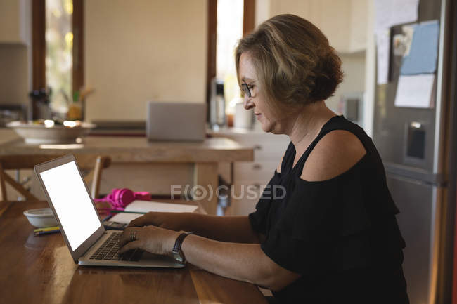 Жінка використовує ноутбук на кухні вдома — стокове фото