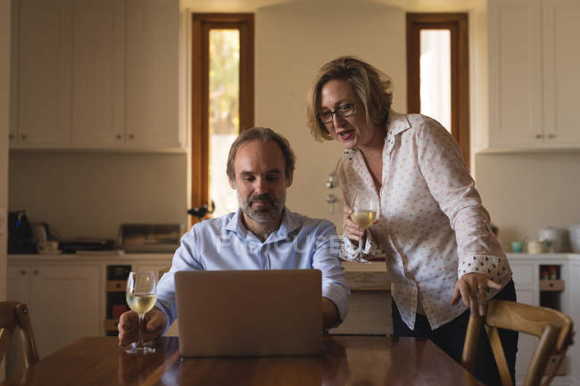 Casal ter champanhe ao usar laptop na cozinha em casa — Fotografia de Stock