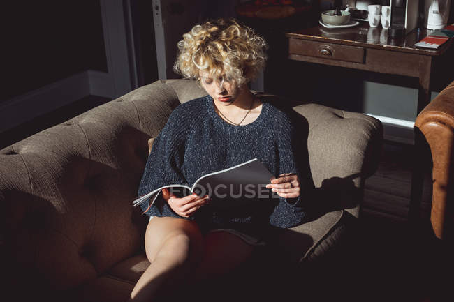 Mulher lendo um livro na sala de estar em casa — Fotografia de Stock