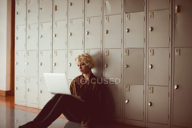 Jeune femme utilisant un ordinateur portable dans les vestiaires à la bibliothèque assis sur le sol — Photo de stock