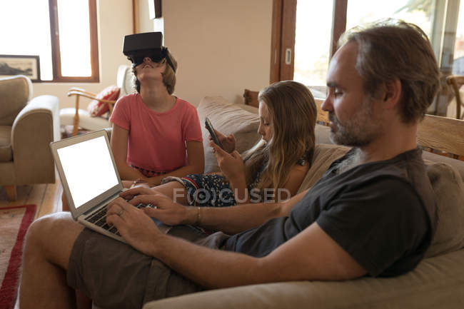 Father and daughters using electronic devices in living room at home — Stock Photo