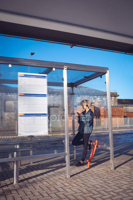 Женщина с мобильного телефона на автобусной остановке в солнечный день — стоковое фото