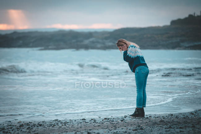 Mujer pensativa de pie en una playa al atardecer - foto de stock