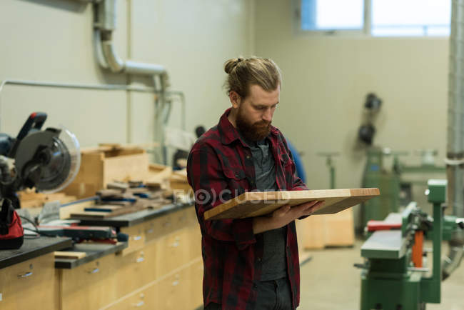 Atento carpinteiro masculino examinando um mobiliário de madeira na oficina — Fotografia de Stock