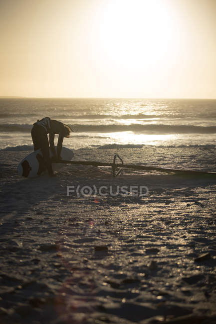 Surfista masculino preparando uma pipa em uma praia ao entardecer — Fotografia de Stock