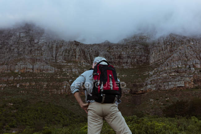 Вид сзади старшего туриста, смотрящего на скалу в сельской местности — стоковое фото