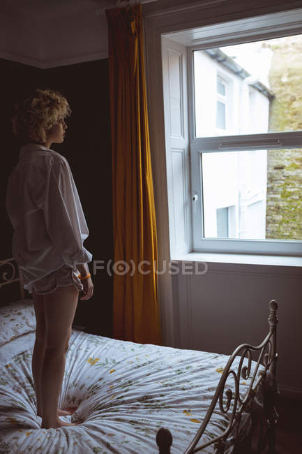 Donna in piedi sul letto in camera da letto a casa — Foto stock