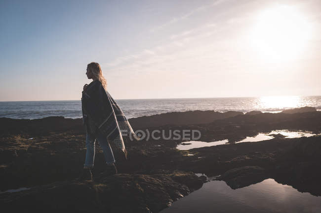 Frau läuft bei Sonnenuntergang über einen Felsen am Strand — Stockfoto