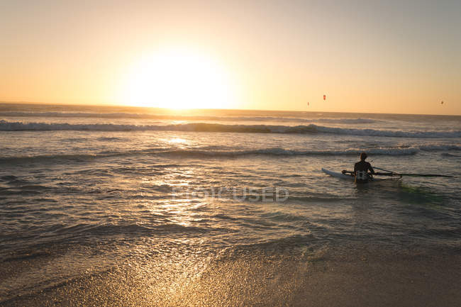 Surfer surft mit Surfbrett in der Abenddämmerung im Meer — Stockfoto