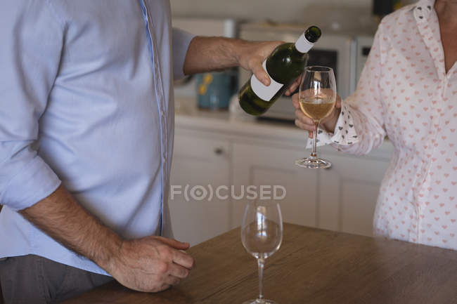 Sezione media dell'uomo versando champagne nel bicchiere a casa — Foto stock
