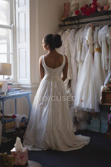 Жінка змішаної раси, наречена в білій сукні дивиться через вікно в бутіку — стокове фото