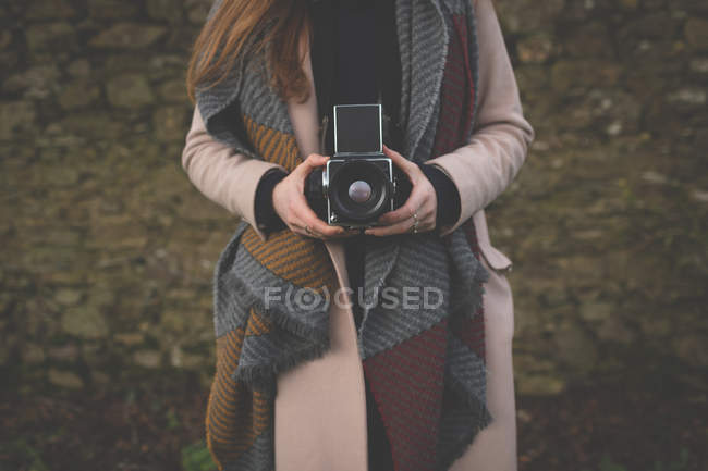Sección media de la mujer tomando fotos con cámara vintage en el campo - foto de stock
