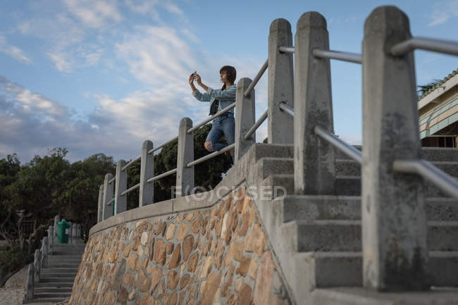Mujer tomando fotos con teléfono móvil en la playa al atardecer - foto de stock