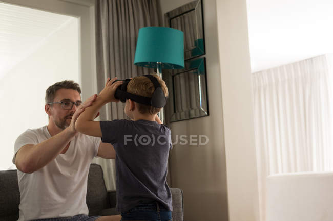 Père aidant son fils à utiliser le casque de réalité virtuelle dans le salon à la maison — Photo de stock