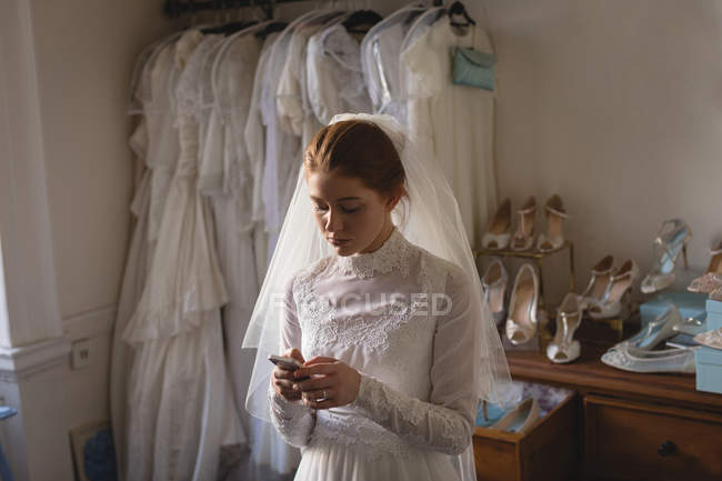 Mariée caucasienne en robe de mariée en utilisant le téléphone mobile dans la boutique — Photo de stock