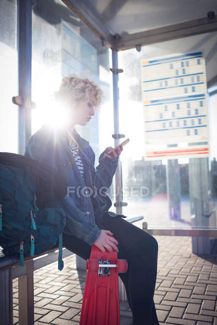 Молода жінка використовує мобільний телефон на автобусній зупинці — стокове фото