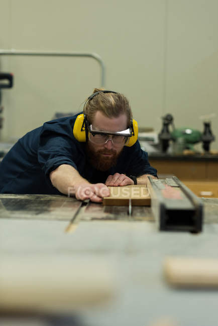 Carpintero macho tomando medidas de madera en taller - foto de stock