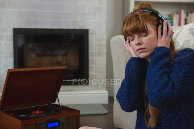Woman in headphones listening to music on gramophone at home — Stock Photo