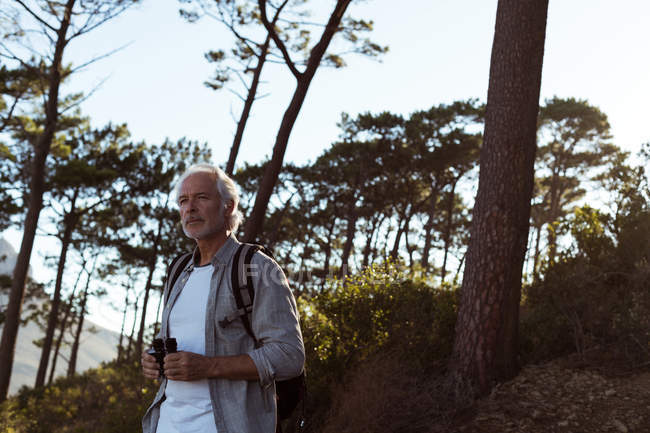 Senior hiker holding binoculars in forest at countryside — Stock Photo