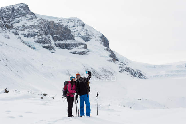 Coppia scattare selfie con cellulare su una montagna innevata durante l'inverno — Foto stock