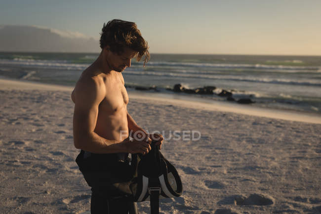 Hombre surfista sosteniendo arnés de cintura en la playa al atardecer - foto de stock