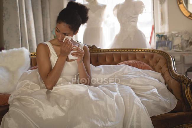 Young bride wiping tears with tissue paper while sitting on sofa — Stock Photo