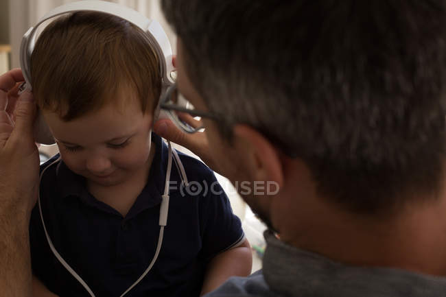 Father and son listening music on headphones at home — Stock Photo
