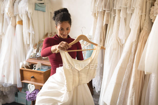 Smiling woman holding wedding dress in clothes hanger at boutique — Stock Photo