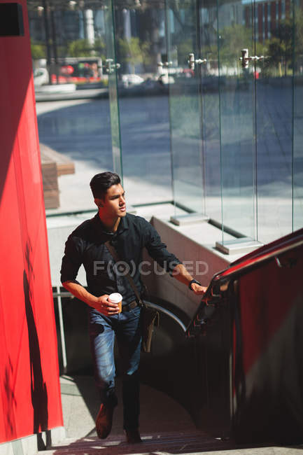 Young businessman moving upstairs while having coffee — Stock Photo