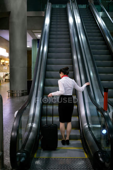Frau steht mit Gepäck auf Rolltreppe am Flughafen — Stockfoto