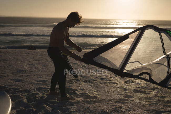 Surfeur masculin préparant un cerf-volant sur une plage au crépuscule — Photo de stock