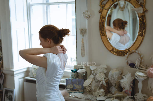 Young bride wearing wedding dress in  boutique and adjusting button on neck — Stock Photo