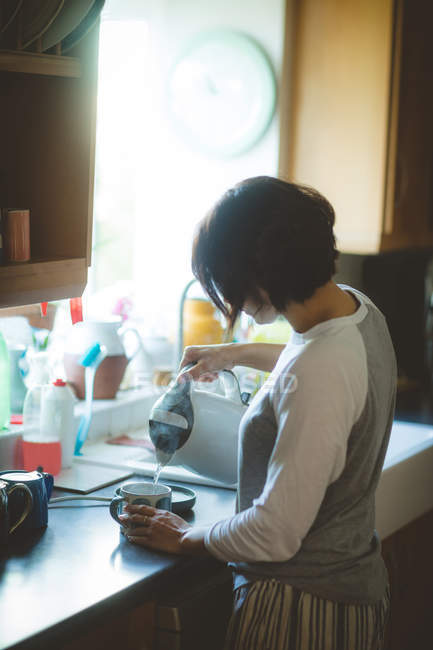 Woman pouring water into mug in kitchen at home — Stock Photo