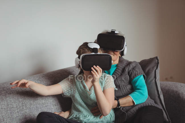 Avó e neta usando fone de ouvido realidade virtual na sala de estar em casa — Fotografia de Stock