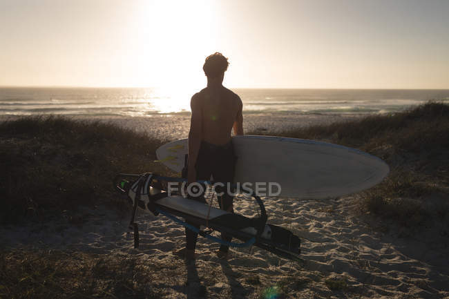 Surfeur masculin debout avec planche de surf sur une plage au crépuscule — Photo de stock
