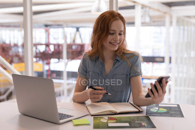 Ejecutiva femenina usando teléfono móvil en el escritorio en la oficina - foto de stock