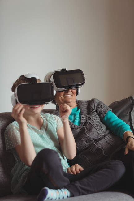 Бабушка и внучка используют гарнитуру виртуальной реальности в гостиной дома — стоковое фото