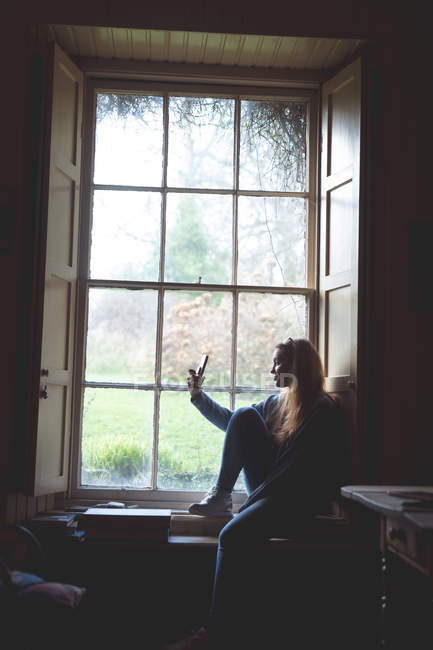 Жінка бере селфі з мобільним телефоном біля вікна вдома — стокове фото